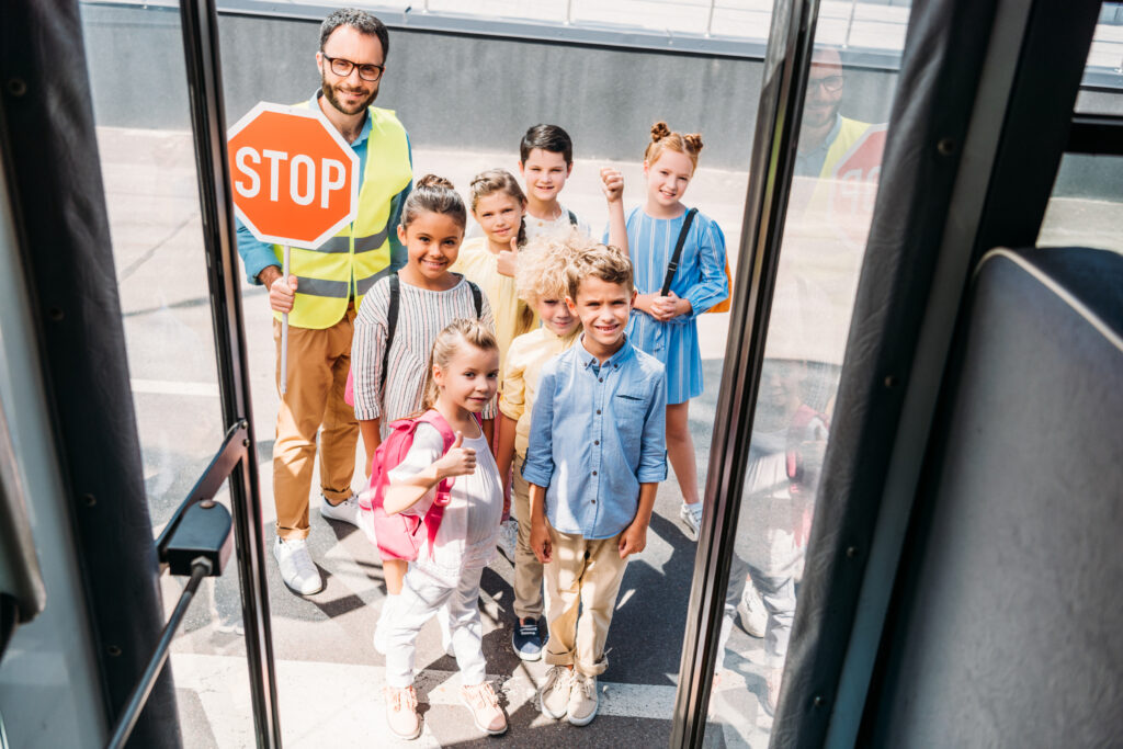 View from a bus at group of happy school children with traffic guard looking at camera